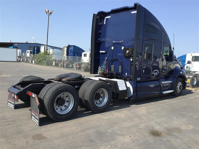 Kenworth T680 tractor in blue, rear view showing dual rear axles and fifth wheel, with aerodynamic sleeper cab and exposed hoses near the back.