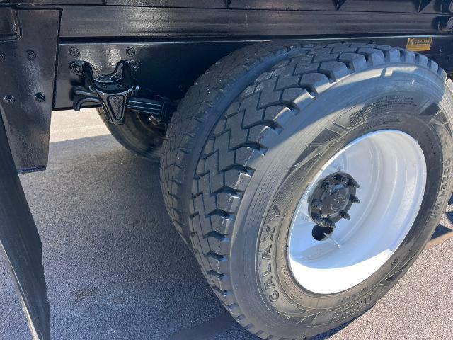 Freightliner M2 106 truck wheel and front suspension showing dual rear? not sure; close-up of front tire with white steel wheel and hub, undercarriage and leaf spring.