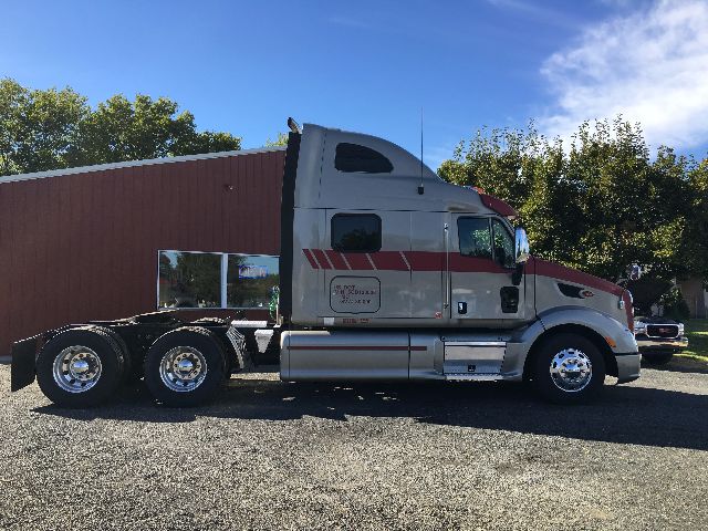 2012 Peterbilt 578 conventional sleeper truck side view with dual rear axles and chrome wheels. Visible text includes company decal on door and reflection in windows.