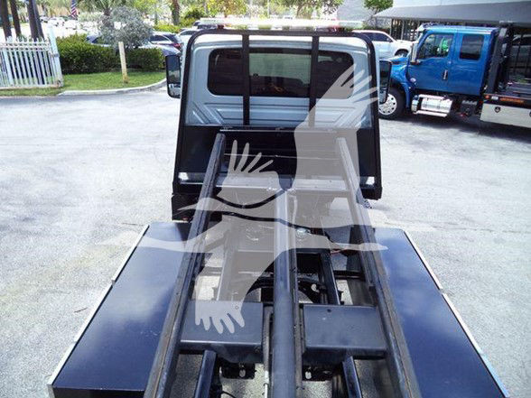 Tow truck chassis with rear view showing hydraulic fork and flatbed rails, International MV cab visible in background.