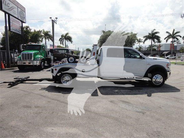 2024 Ram 5500 SLT tow truck in a dealership lot, white crew cab with extended cab and a tow hitch. Palm trees in background.
