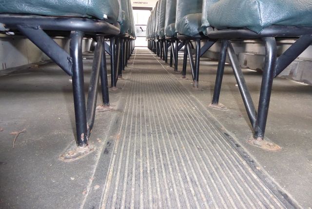 Bus interior floor view between rows of seats showing aisle with ribbed flooring and metal legs of seats