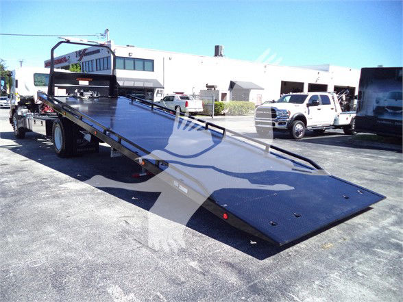Isuzu FTR flatbed tow truck with a long hydraulic ramp in a dealership lot.