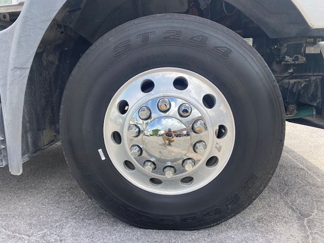 Truck front wheel showing ST24 tire and shiny steel hubcap with lug nuts. Reflection in hubcap.