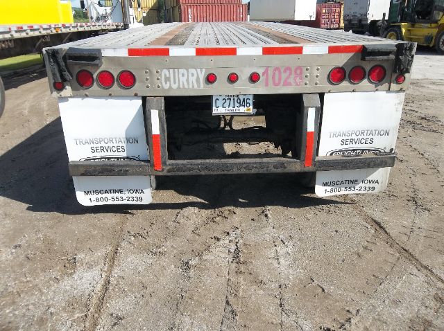 Rear view of a flatbed trailer with red and white reflective tape, spare mudflaps reading Transportation Services Muscatine Iowa, and license plate visible.