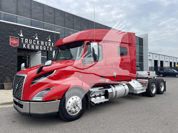 Volvo VNL64T740 tractor unit in red with sleeper cab parked in front of a dealer, showing front grille, chrome bumper, and side fuel tanks.