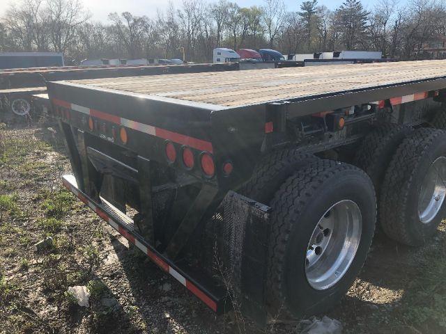 Load King PF 948 oilfield flat deck trailer rear/side view with dual rear axles and wood deck. Visible tags and reflectors along the side.