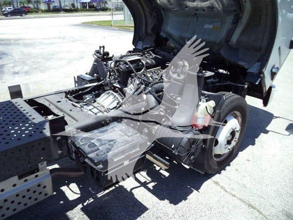 Isuzu NQR truck chassis with open cabin area showing engine bay and transmission, rear wheel, and various components.