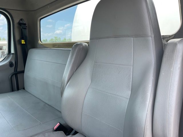 Truck cab interior showing grey vinyl seats and side window. Front bench seat and passenger seat visible with seat belts.