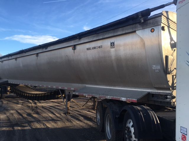 Trailer side showing Model ASHR 2 487248 on a long silver hopper trailer with dual rear axles and landing gear, under clear sky.