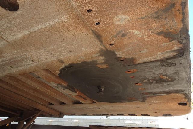 Underbody view of a trailer floor with rust and a circular patched area near the center.