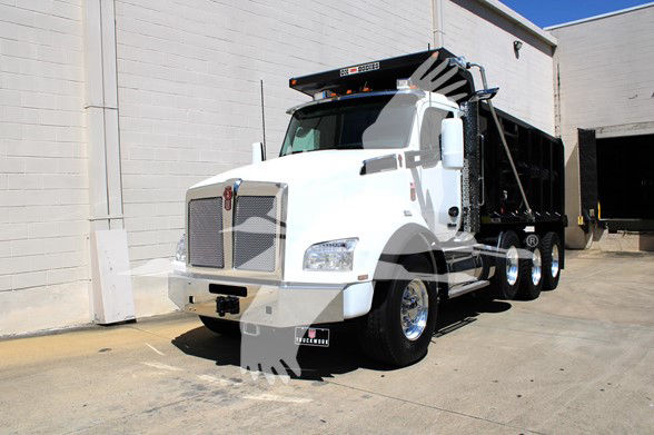 White 2026 Kenworth T880 dump truck in an industrial setting, chrome grille, large side mirrors, black dump bed, and roof-mounted light bar.