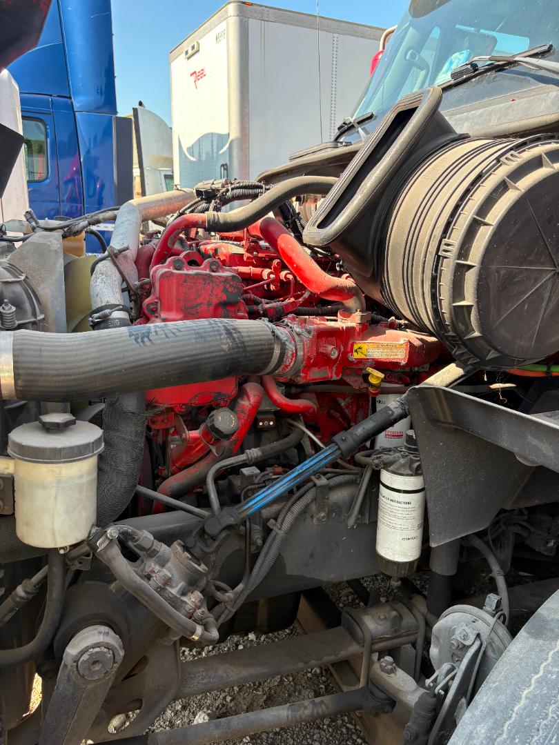 Tractor-trailer engine bay of a 2016 International Prostar with red engine, hoses, and filters visible; air intake tube and coolant reservoir present.