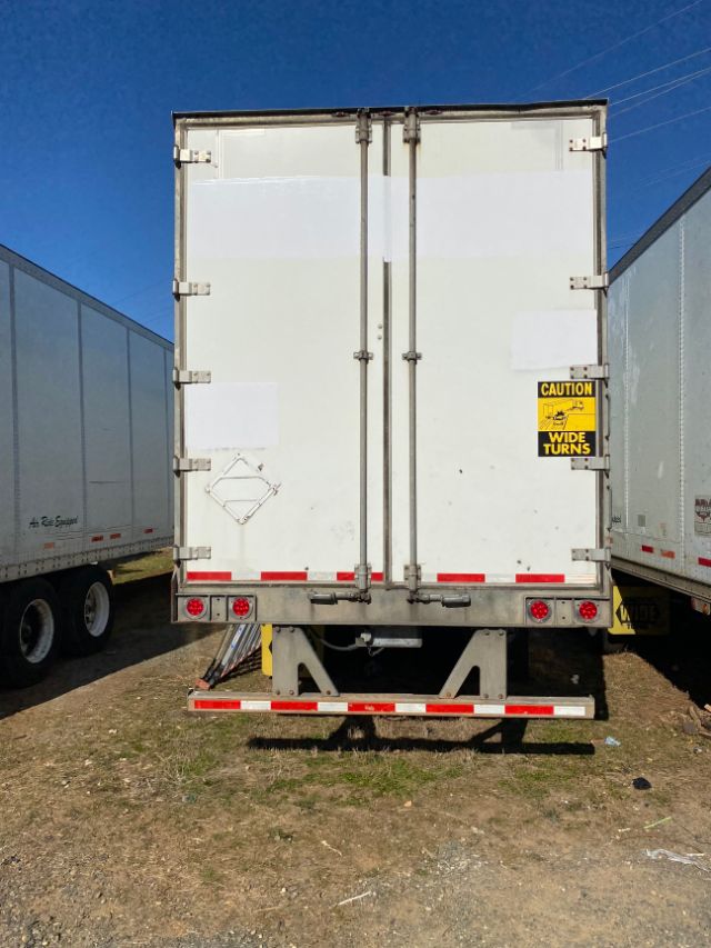 Rear view of a white 2015 Wabash Duraplate trailer with twin doors, CAUTION sign, red/white reflective tape, and rear underride guard.