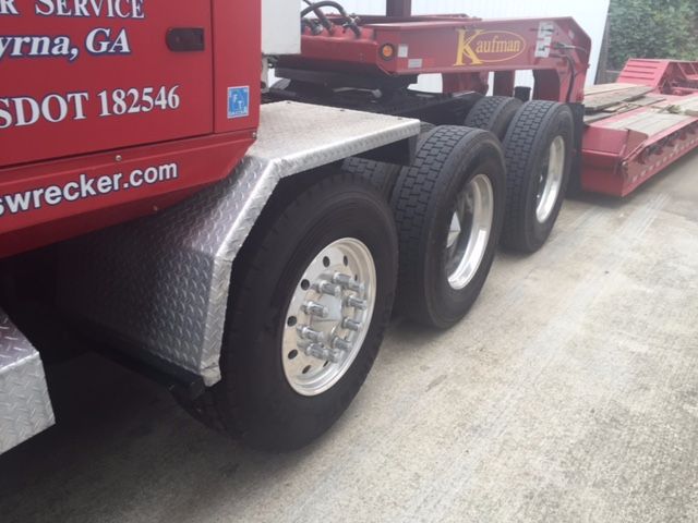 Truck wheel area of a red Western Star 4900fa with alloy wheels and multiple rear axles, decals read 'Kaufman' crane equipment and 'swrecker.com' on the side.