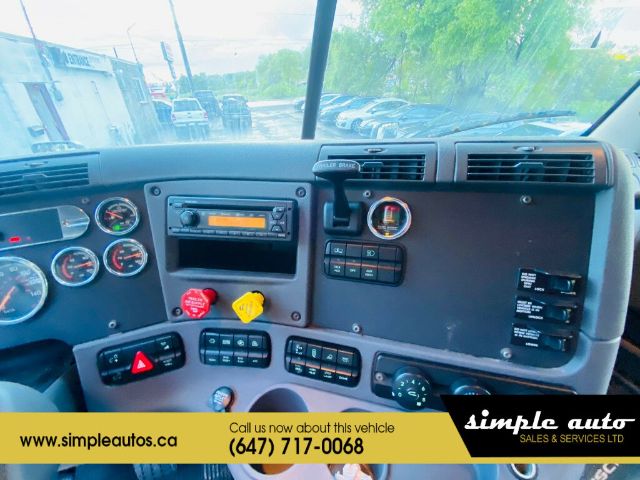 Dashboard of a Freightliner Cascadia truck showing gauges, steering column, and center console with radio, knobs, and warning lights. Promotional banner across bottom with website and phone number.