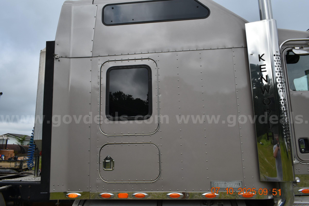 Kenworth W900 cab and chassis rear side showing polished exhaust stack, riveted metal body, and rear windows.