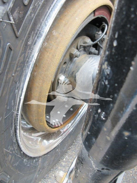 Volvo VNL wheel showing hub, brake assembly, and worn tire with tan sidewall; front fender and shock area visible.