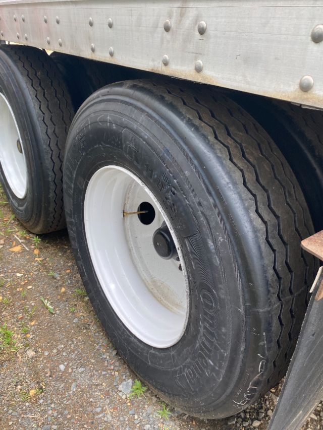 Dual rear trailer wheels with solid black tires and white steel rims under a Duraplate trailer side shell.