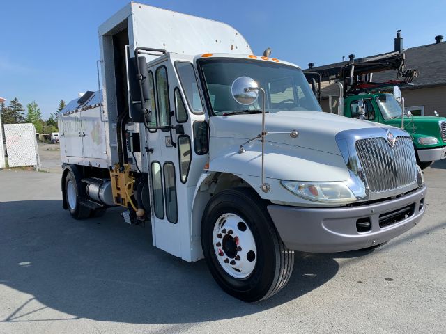 International 4300 garbage truck side/front view showing cab and body with chrome grille and white paint.