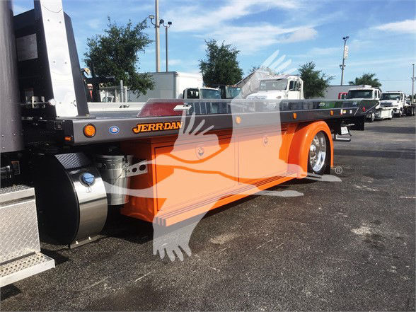Peterbilt 337 flatbed tow truck in orange with Jerr-Dan branding, side view showing long flatbed and rear wheels, dealership lot in background.
