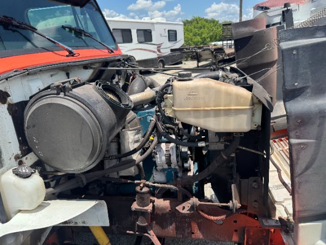 International DT 466E engine bay showing coolant reservoir, air intake, and various hoses with a rusty frame. Front view of truck engine compartment.