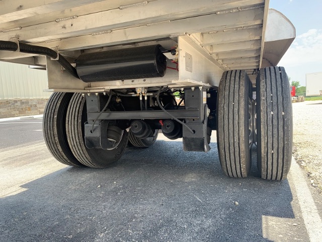 Aluminum end dump trailer underside showing dual rear axles and suspension, with tires and underbody hardware visible.