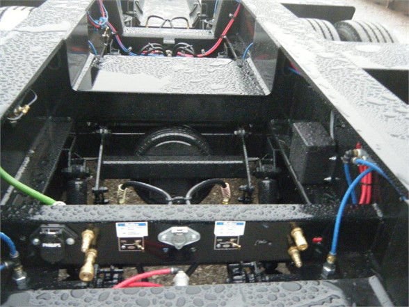 Talbert 55SA flat level deck HRG trailer undercarriage showing hydraulic lines, batteries, wiring, and connection valves with textured metal deck.