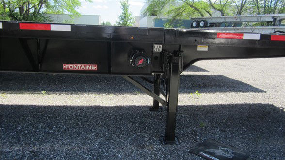 Fontaine flatbed trailer undercarriage showing Fontaine brand label and support leg with stabilizer. Deck edge with reflective tape.