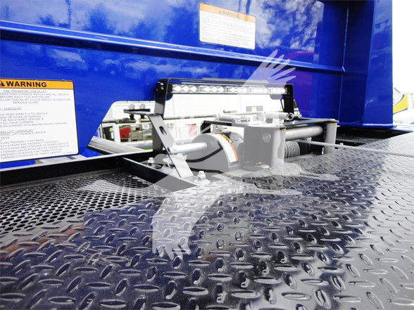 Truck bed area showing a hydraulic or hitch mechanism mounted on a textured diamond plate surface. There are warning labels and a blue body panel in the background.