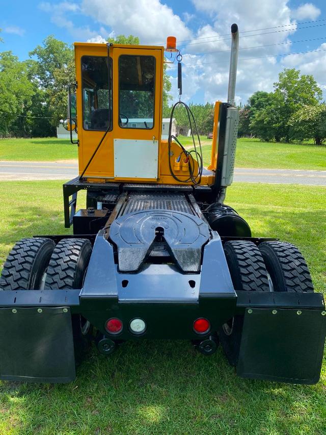 Yellow yard spotter tractor cab with black chassis, showing rear view with dual rear tires and taillights.