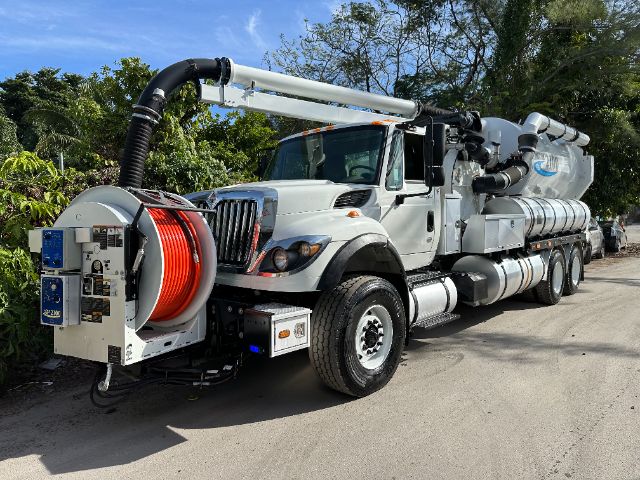 Industrial vacuum truck with large white cab and rear-mounted vacuum tank, hose reel on front left with bright red hose, long articulating suction arm extending over cab.