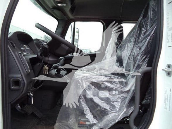 cab interior of a Freightliner truck showing driver seat covered in plastic, steering wheel, dashboard, pedals, and door frame.
