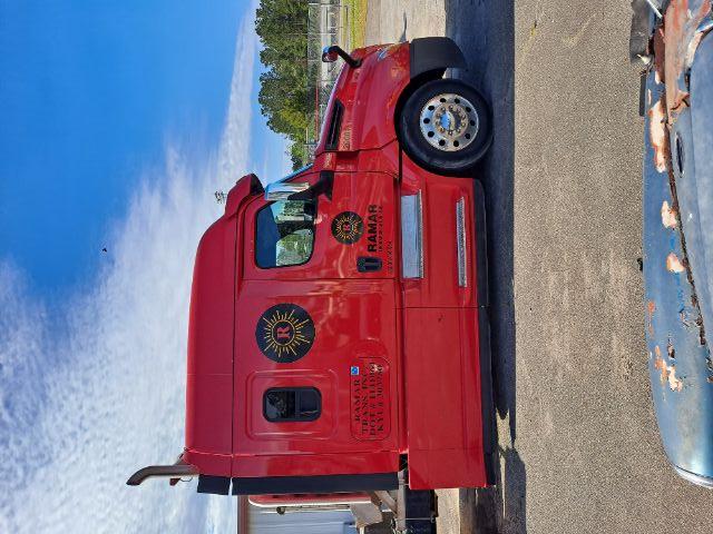 Red Freightliner Cascadia tractor side view showing sleeper cab, chrome wheels, RAMAR logo, and fuel/air components on the side; text stickers on door and panels.