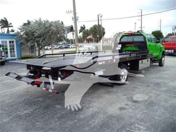 Flatbed tow truck chassis with green cab, rear flatbed, and license plate lights visible.