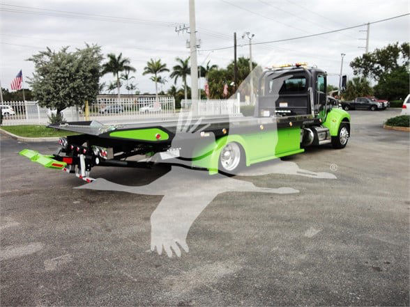 Tow truck with green and black color scheme, Peterbilt 337, rear flatbed and winch apparatus visible.