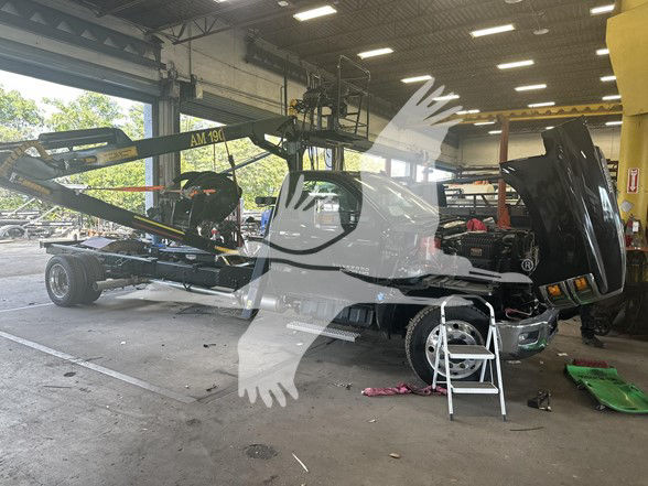 Truck in shop with crane attachment and open hood; image shows a Chevrolet Silverado 6500HD chassis cab in a repair bay.