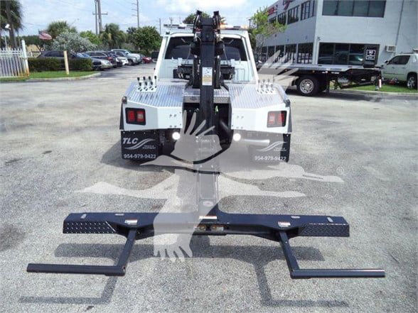 Front view of a white Ram 5500 tow truck with a heavy-duty hitch/towing apparatus attached in the bed area; visible text on rear panels includes TLC 954-479-942? and 954-479-? on both sides.