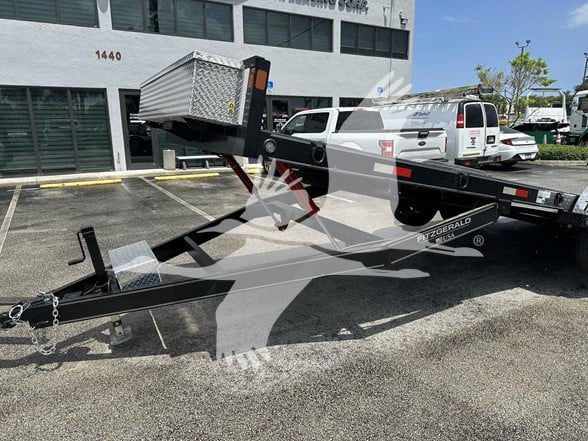 Flatbed trailer with 24 ft length showing gooseneck coupler, steel frame, hitch chain, and deck toolbox at front.