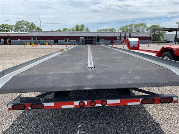 Flatbed trailer with drop deck and tandem axles, viewing from rear showing rubberized loading surface and center rails.