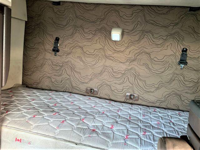 Interior sleeper bunk area with beige patterned wall and quilted mattress; there are two hooks on the wall and a small light/handle in the center.