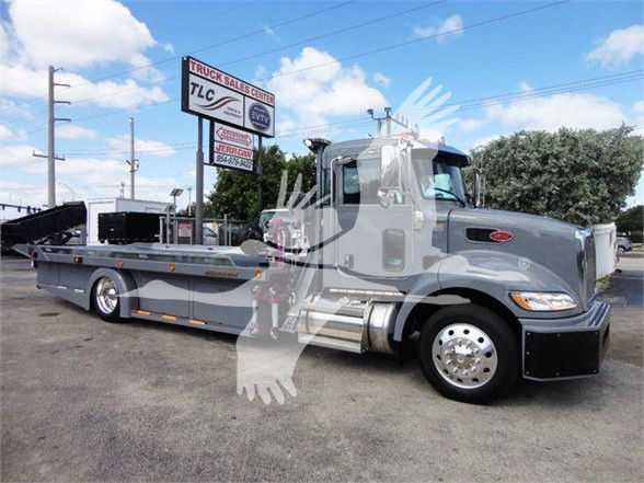 Peterbilt 337 tow truck in a lot with a long flatbed, gray paint, cab and sleeper area visible.