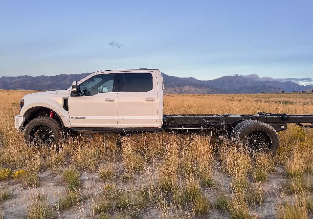 Ford F-550 Lariat cab and chassis in a field, white crew cab with long chassis and black rails