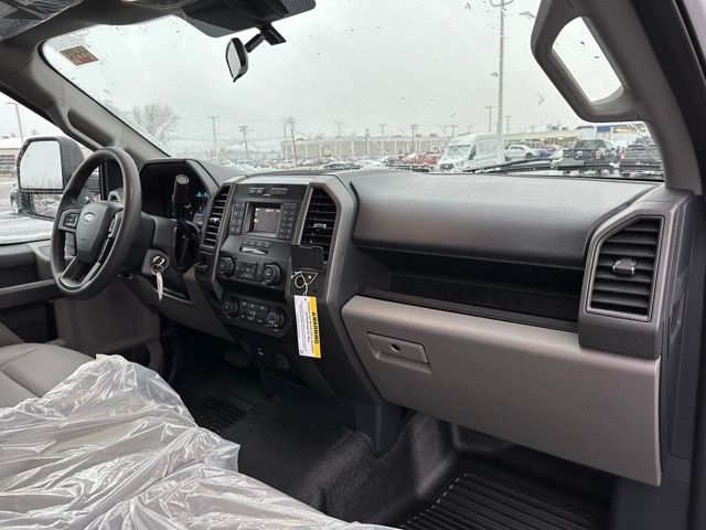 Truck interior showing steering wheel, dashboard, center console with touchscreen, gear selector, and plastic seat covering.