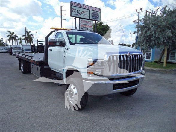 Truck with a flatbed tow body and missing front wheel shows chrome grille and light bar on roof.